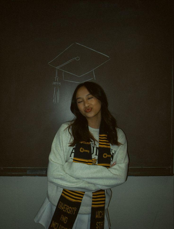 a young woman standing in front of a chalkboard with a graduation cap on it