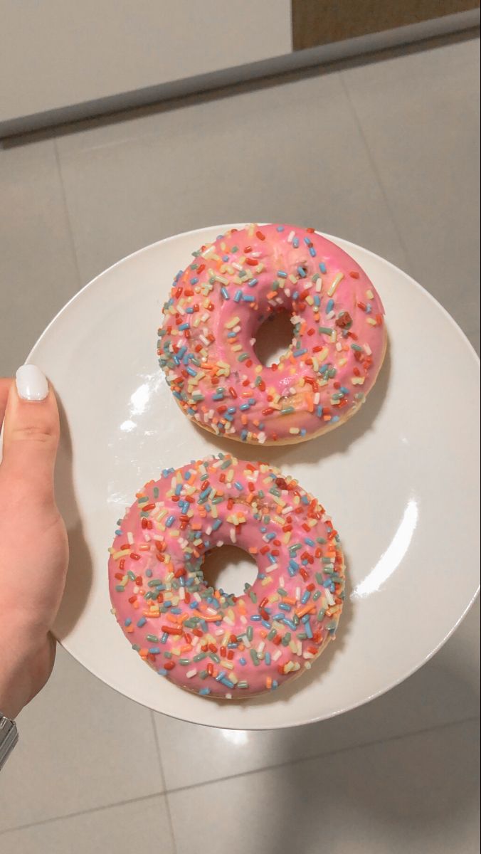 two glazed donuts with sprinkles on a white plate, being held by a person