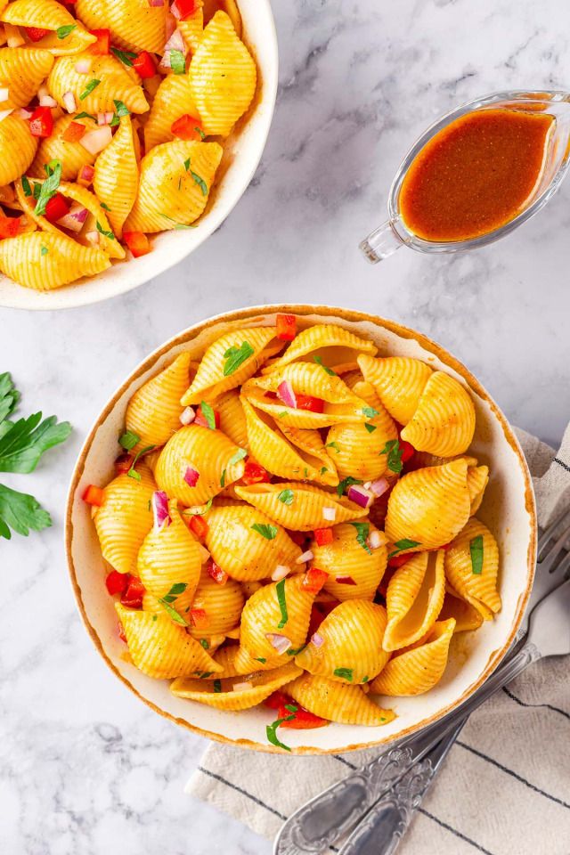 two bowls filled with pasta and sauce on top of a marble countertop next to silverware