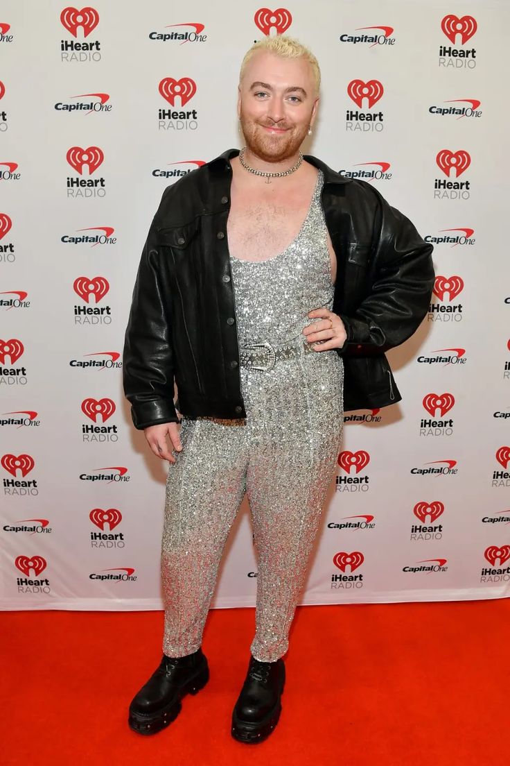 a man with blonde hair wearing silver pants and black jacket standing in front of a red carpet