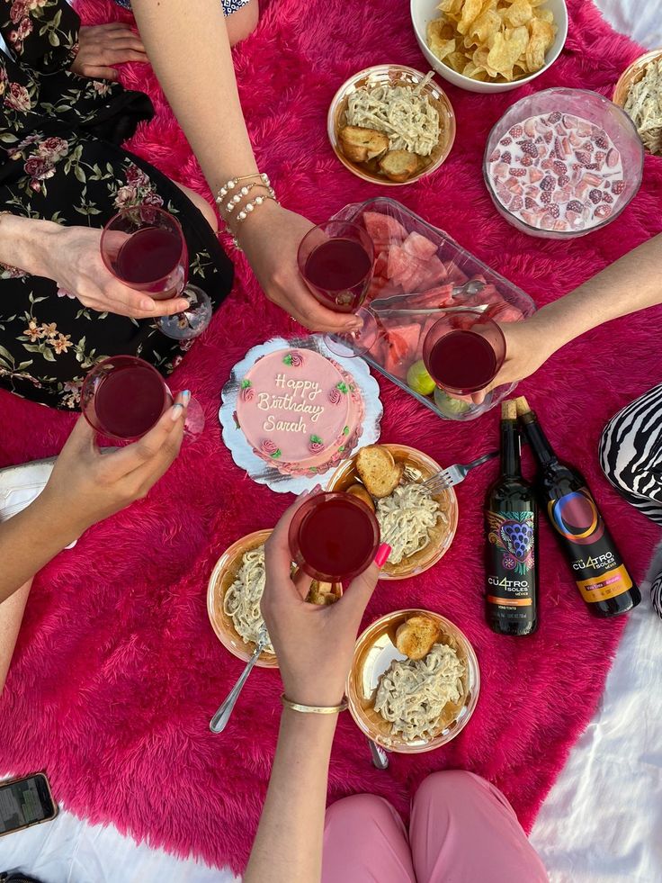 several people toasting with wine and food on a pink rug in front of them