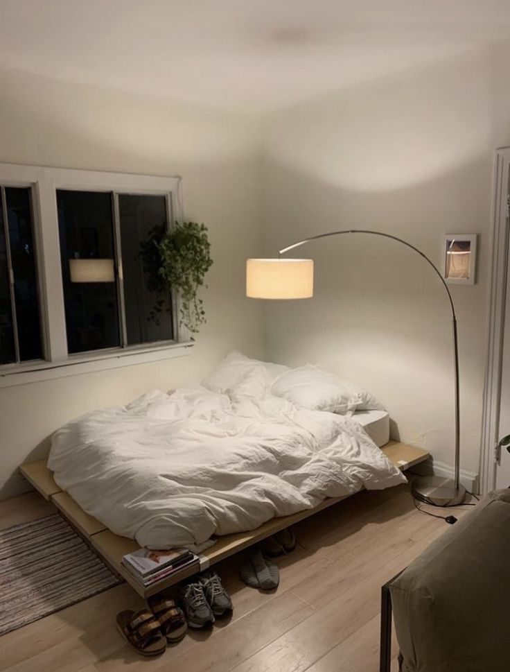 an unmade bed sitting on top of a hard wood floor next to a window