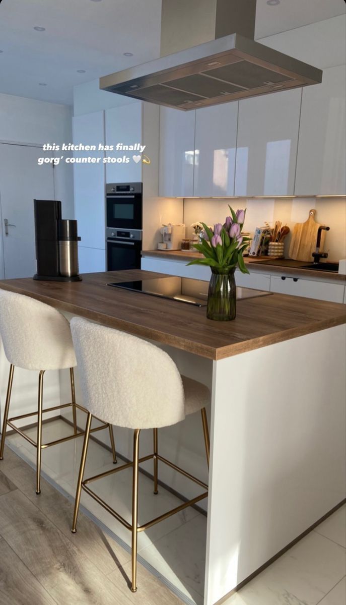 a kitchen with white cabinets and wooden counter tops is shown on the phone screen, while three stools sit at the center of the island