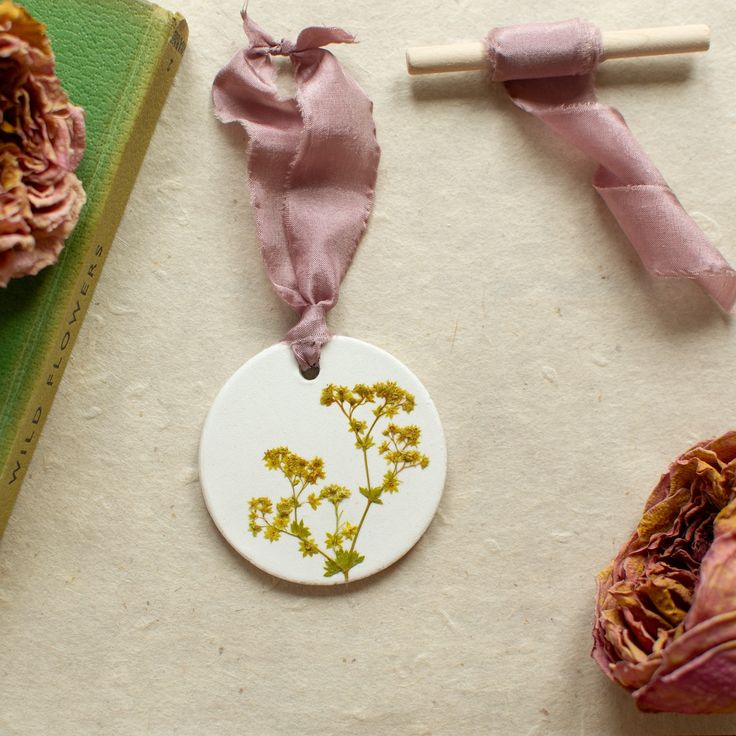 some dried flowers are sitting on a table next to a book and a pink ribbon