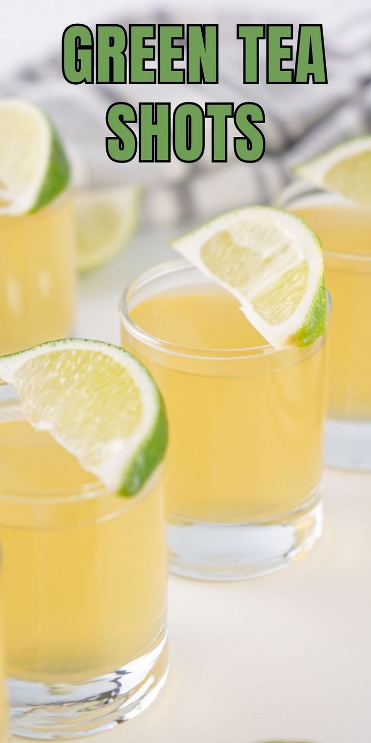 three glasses filled with green tea shots on top of a white table next to limes