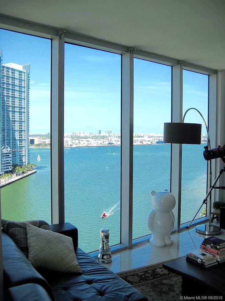 a living room filled with furniture and large windows overlooking the water in front of it