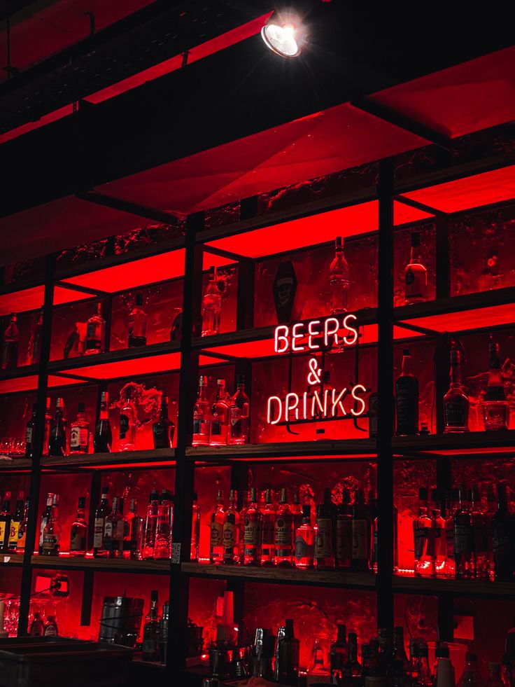 a bar with red lights and liquor bottles on the shelves that are filled with drinks