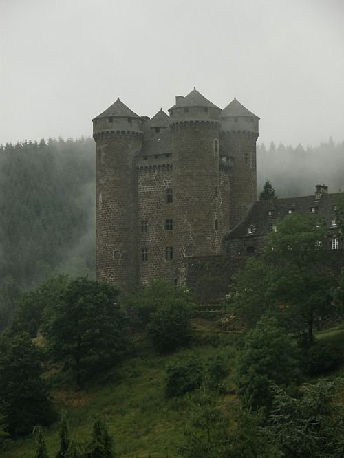 an old castle sitting on top of a lush green hillside covered in fog and mist