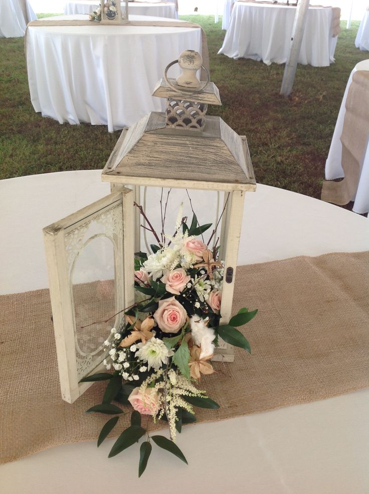 a lantern with flowers and greenery is on the table at an outdoor wedding reception