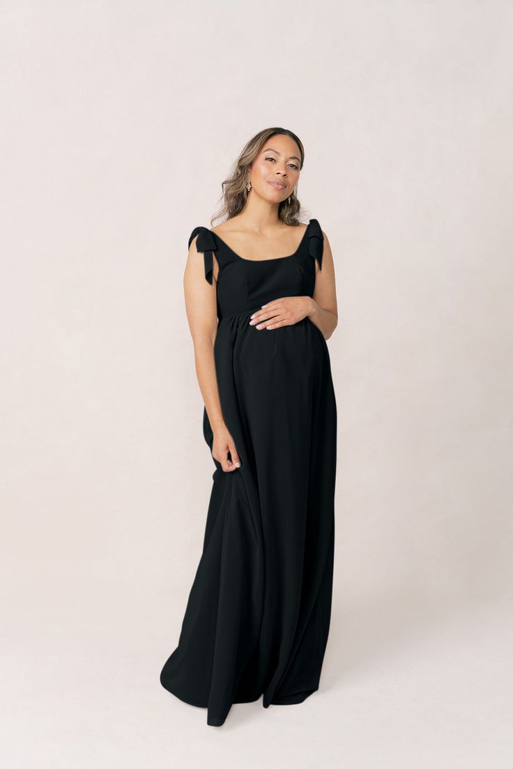 a pregnant woman in a black gown poses for the camera with her hands on her belly