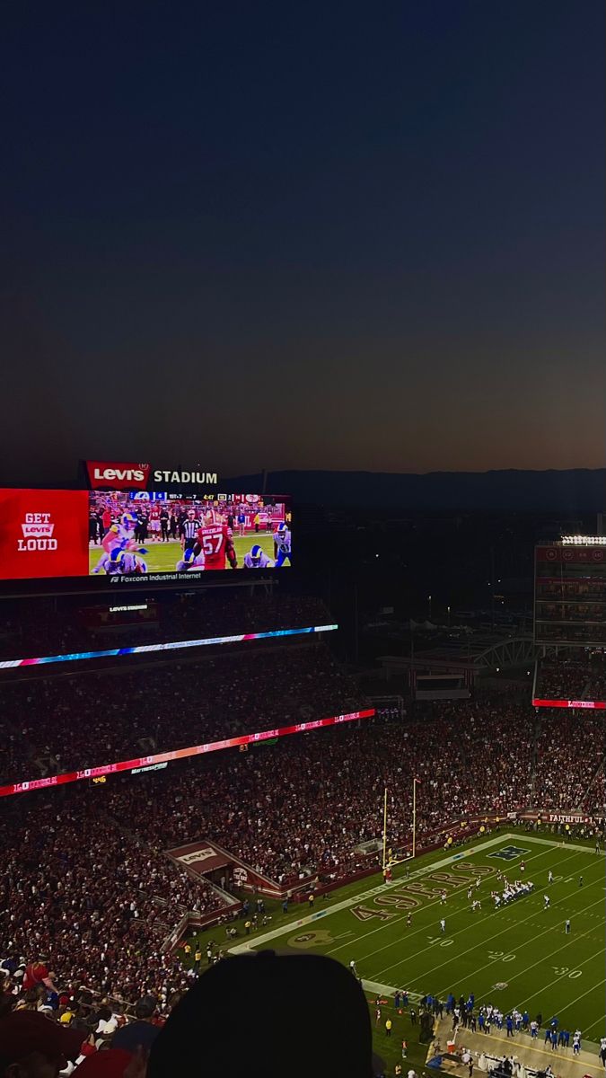 a stadium filled with lots of people watching a football game on the big screen tv