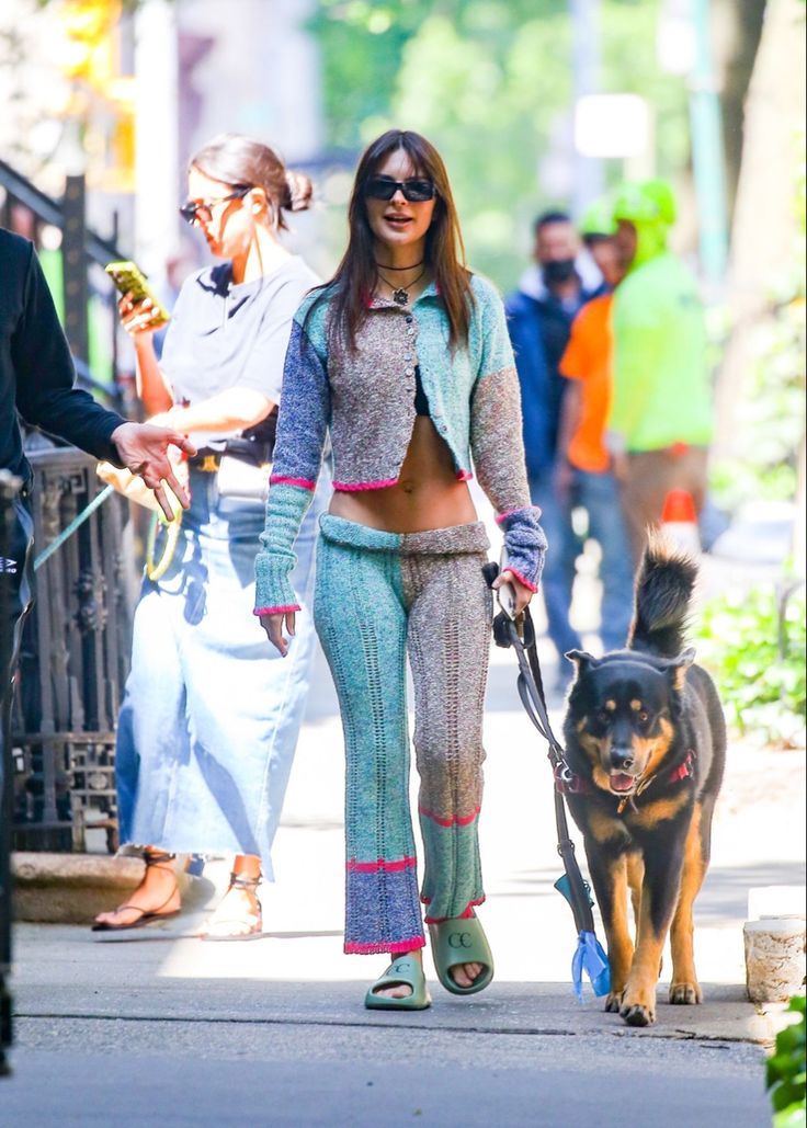 a woman walking her dog down the street with other people in the background on a sunny day