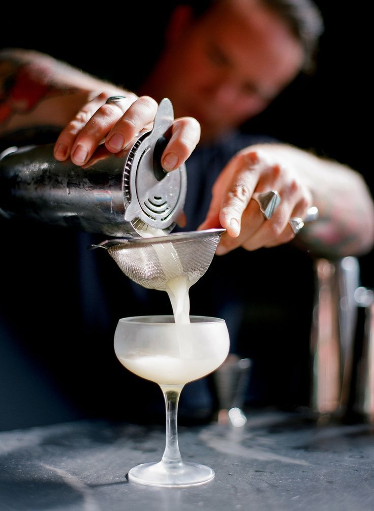 the bartender is making a drink at the bar with his hand on the shaker