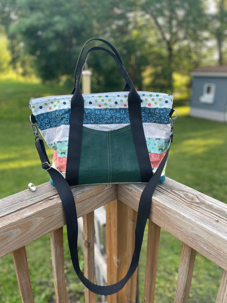 A handcrafted tote bag perfect for everyday use; travel, work, and school.  Exterior front slip pocket. One large interior slip pocket Materials: Nylon webbing handles and crossbody strap. Cork front pocket and cork bottom. Special Features: * Main body is a fun assortment of frogs and polka dot pattern  * Lining is super soft cotton * 1-1/2" nylon webbing for handles and shoulder strap, approximately 56" long Finished size is approximately 15" wide x 12" tall x 5" deep Pattern is Oxbow Tote by Noodlehead. Casual Weekender Bag With Adjustable Strap For Everyday Use, Green Weekender Bag With Adjustable Strap For Everyday Use, Green Weekender Bag With Adjustable Strap, Green Satchel With Adjustable Handle For Everyday, Green Everyday Diaper Bag With Adjustable Strap, Green Diaper Bag With Adjustable Strap, Green Diaper Bag With Adjustable Strap For Everyday Use, Everyday Green Diaper Bag With Adjustable Strap, Green Tote Diaper Bag For Everyday Use