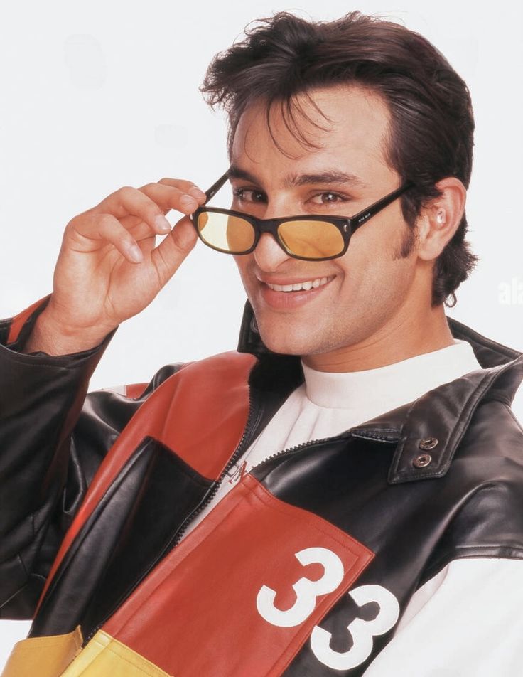 a man in a leather jacket and sunglasses holding up his eyeglasses to the camera