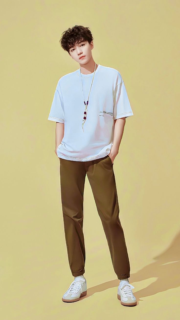 a man standing in front of a yellow background wearing brown pants and a white t - shirt