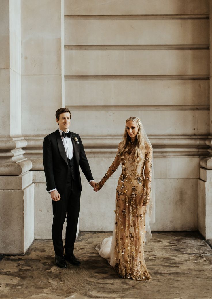 a man in a tuxedo and a woman in a long dress holding hands