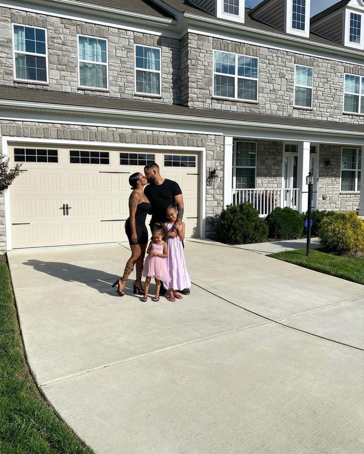 a woman and two children standing in front of a large house with garage doors on both sides