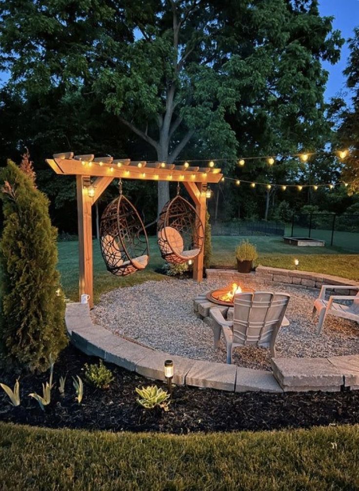 an outdoor patio with lights and chairs around the fire pit, surrounded by landscaping materials