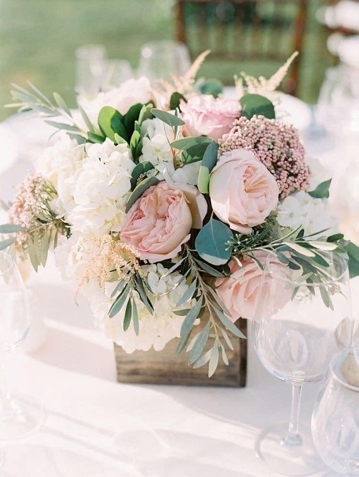 a vase filled with pink and white flowers sitting on top of a table next to wine glasses