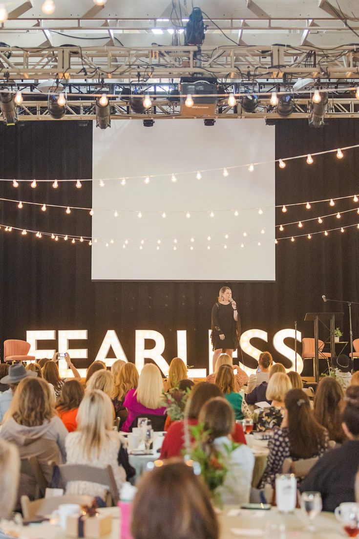 people sitting at tables in front of a screen with the word fearless on it and lights strung above them