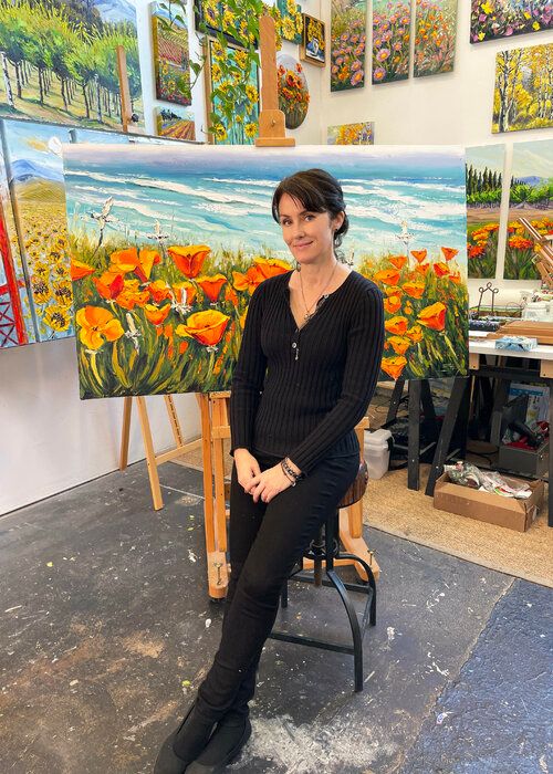 a woman sitting on a chair in front of an easel with paintings behind her