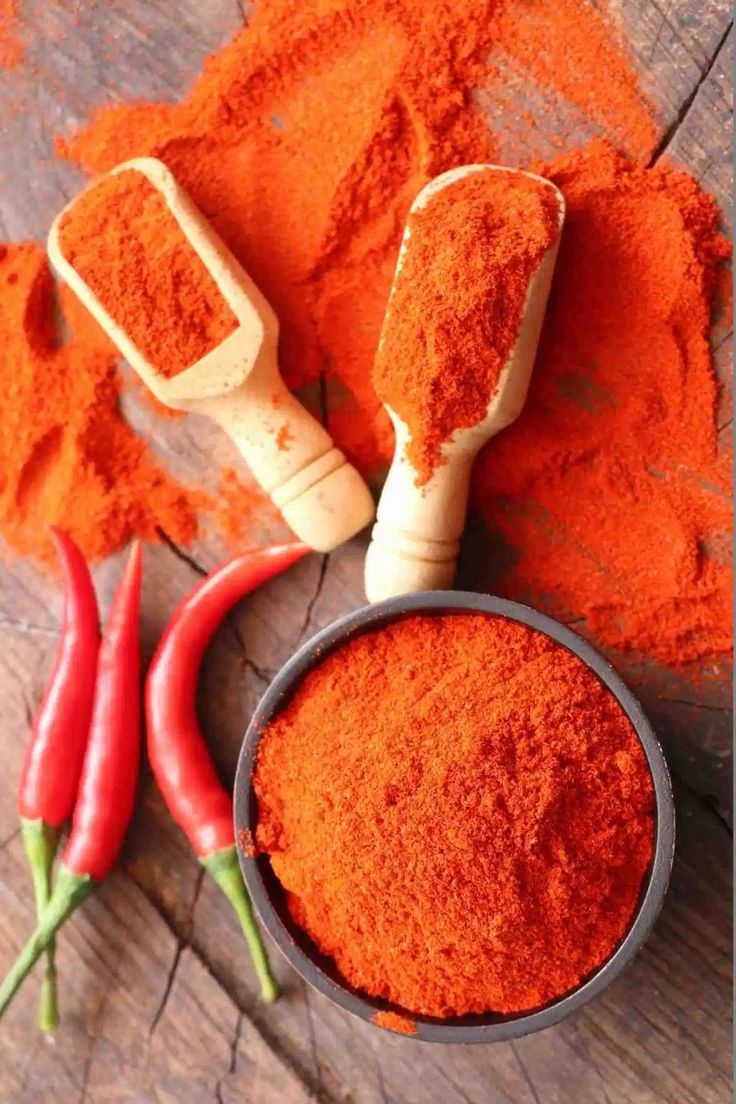 red chili powder in a bowl next to two peppers