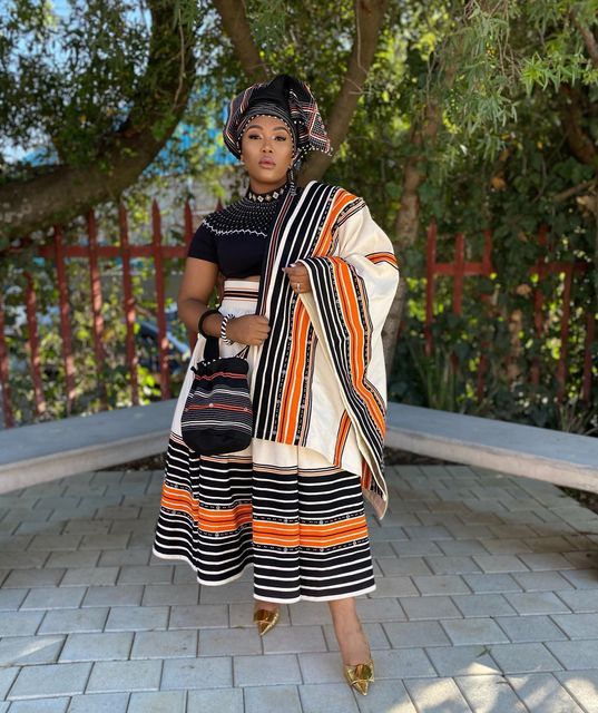 a woman standing on a brick walkway wearing a black and white dress with orange stripes