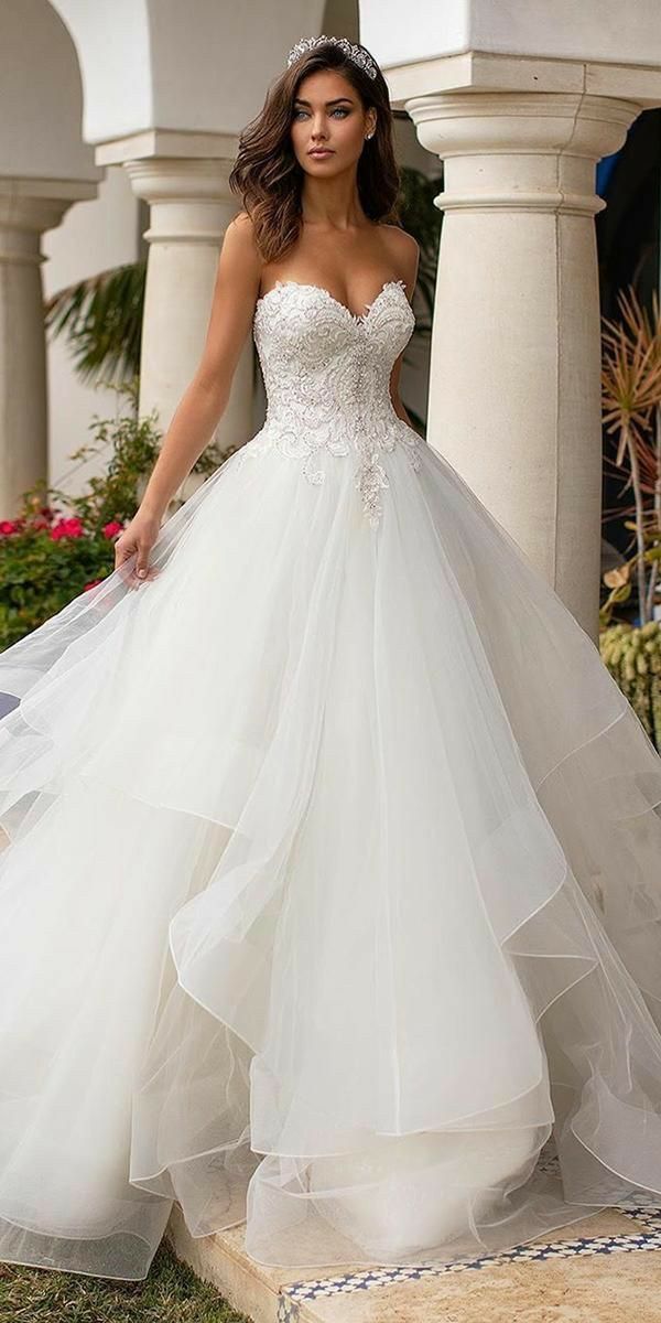 a woman in a white wedding dress is standing on the steps outside with her arms behind her back