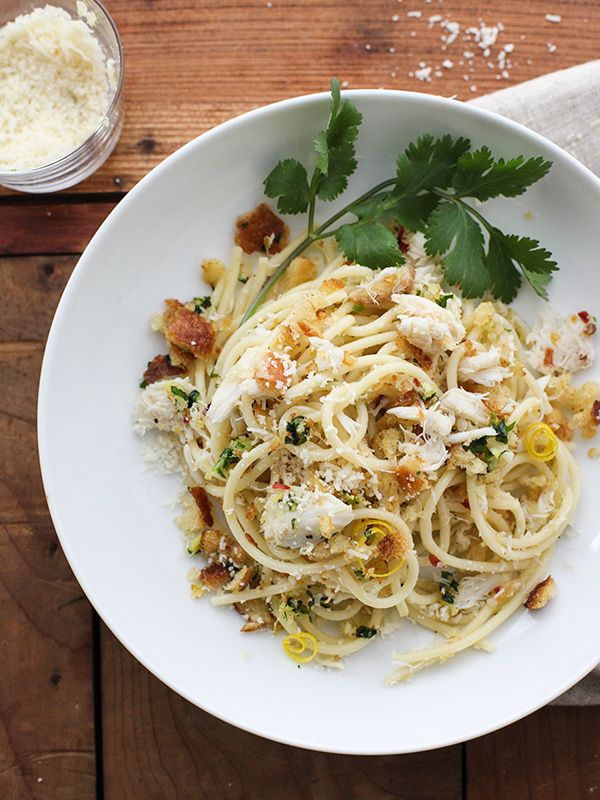 a white bowl filled with pasta and garnished with parsley on top of a wooden table