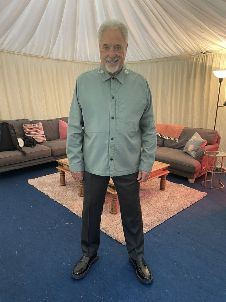 an older man standing in front of a couch and chair with his hands in his pockets