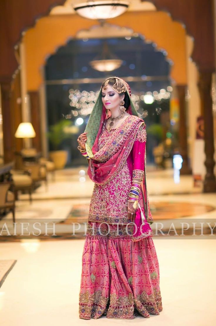 a woman in a pink and green bridal gown posing for the camera with her hand on her hip