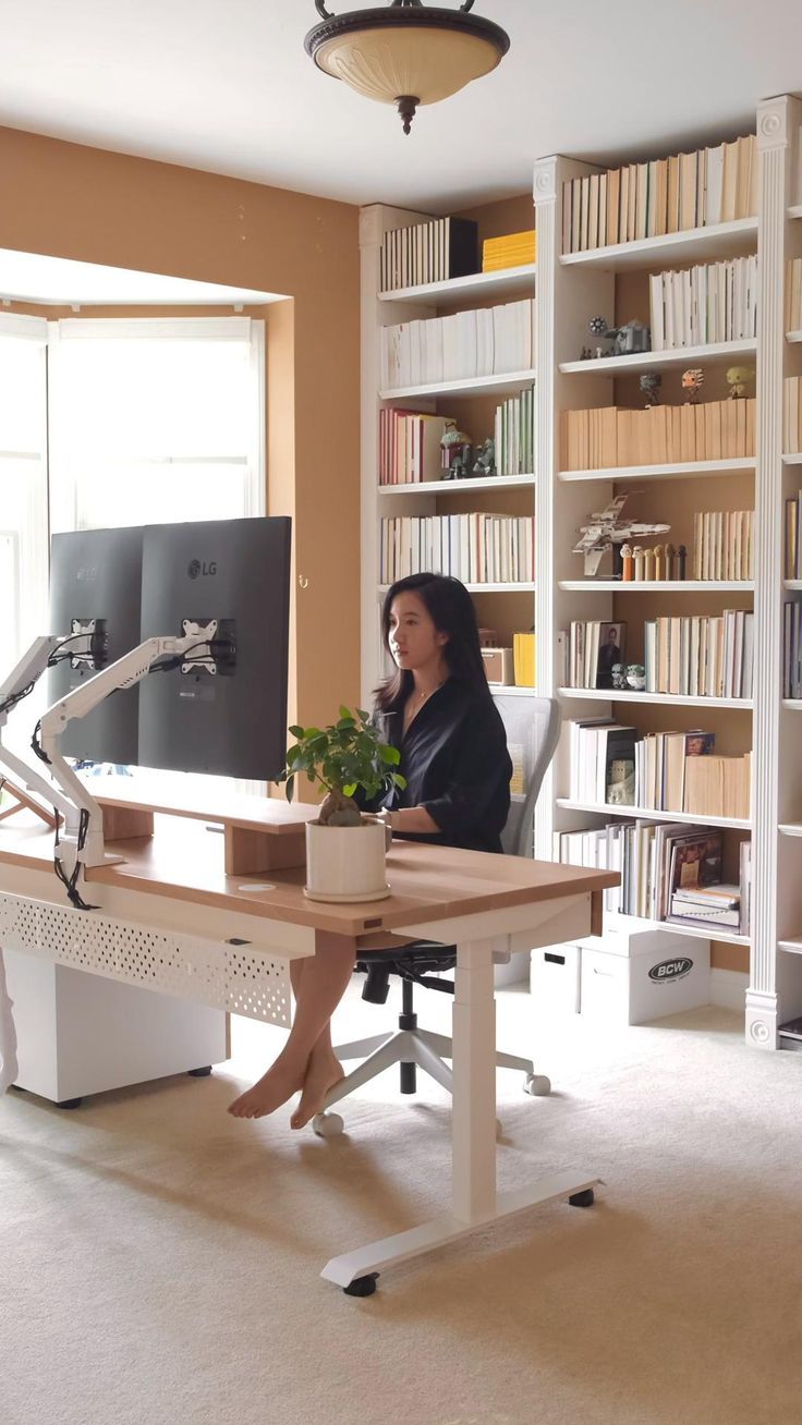 a woman sitting at a desk in front of a computer monitor and bookshelf