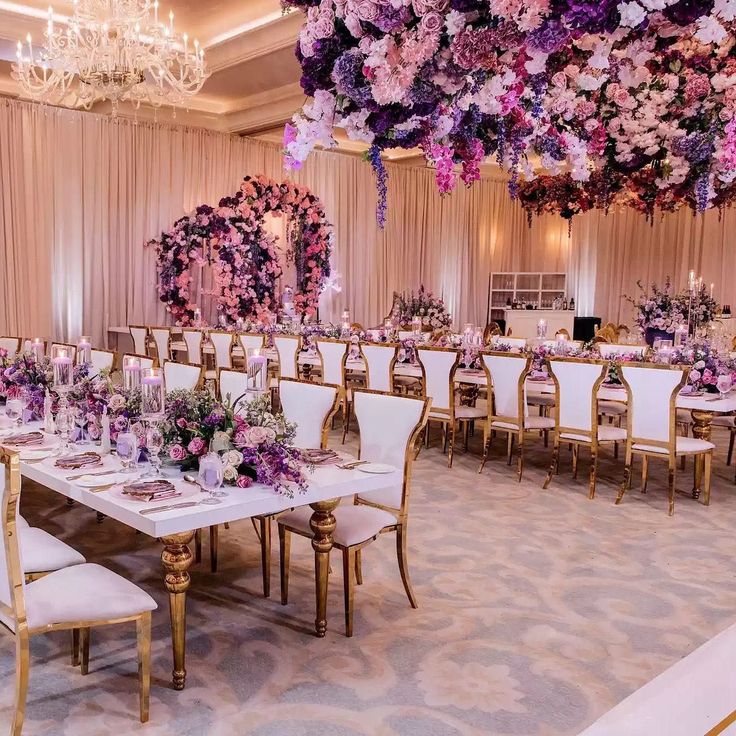 a dining room with tables and chairs covered in purple floral arrangements hanging from the ceiling