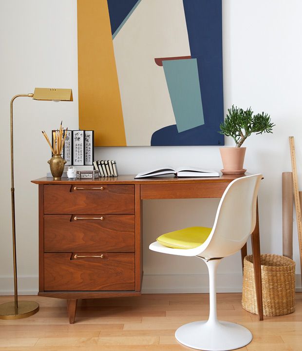 a desk with a yellow chair and a painting on the wall above it in an office