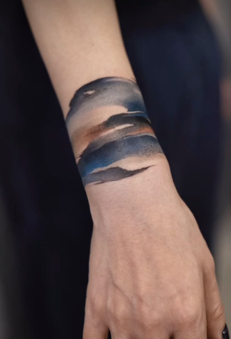 a woman's hand with a tattoo on her wrist that has clouds in the sky