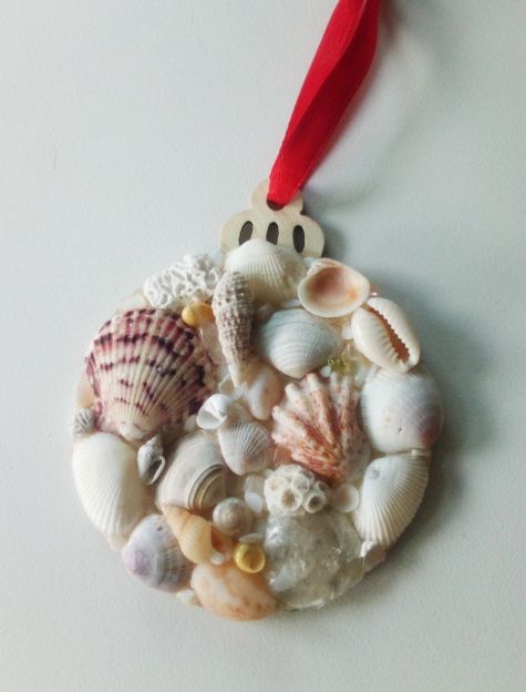 a christmas ornament with seashells and shells hanging from a red ribbon