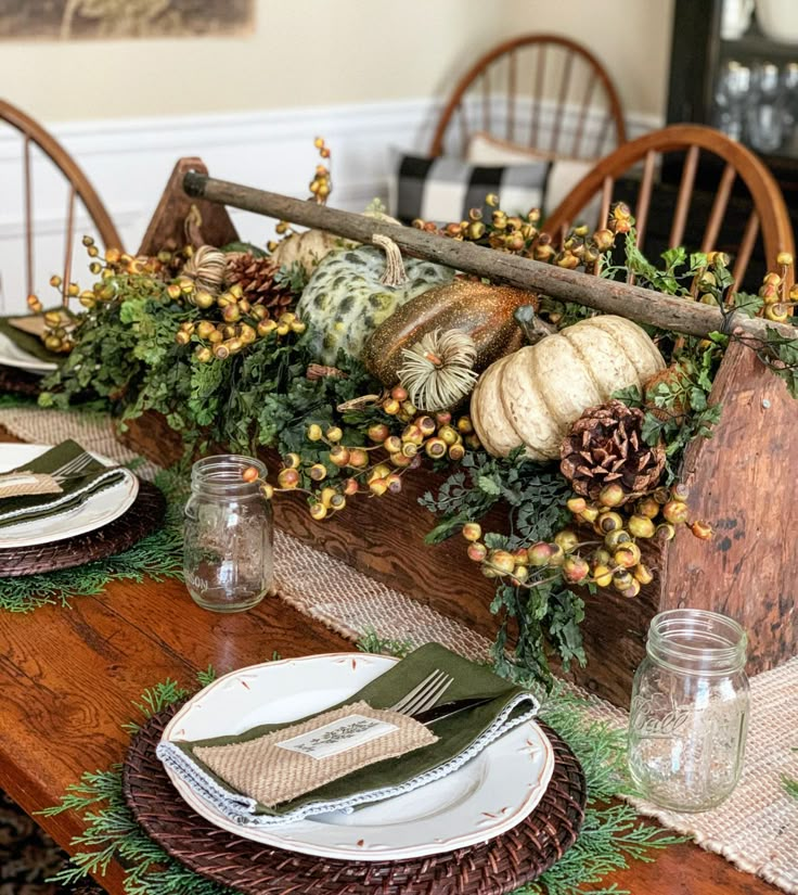 the table is set for thanksgiving dinner with pine cones and pumpkins on it, along with greenery