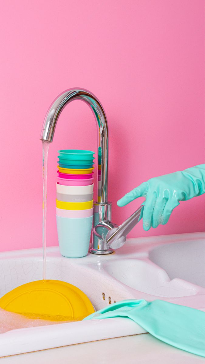 a person in blue gloves washing dishes under a faucet on a pink wall