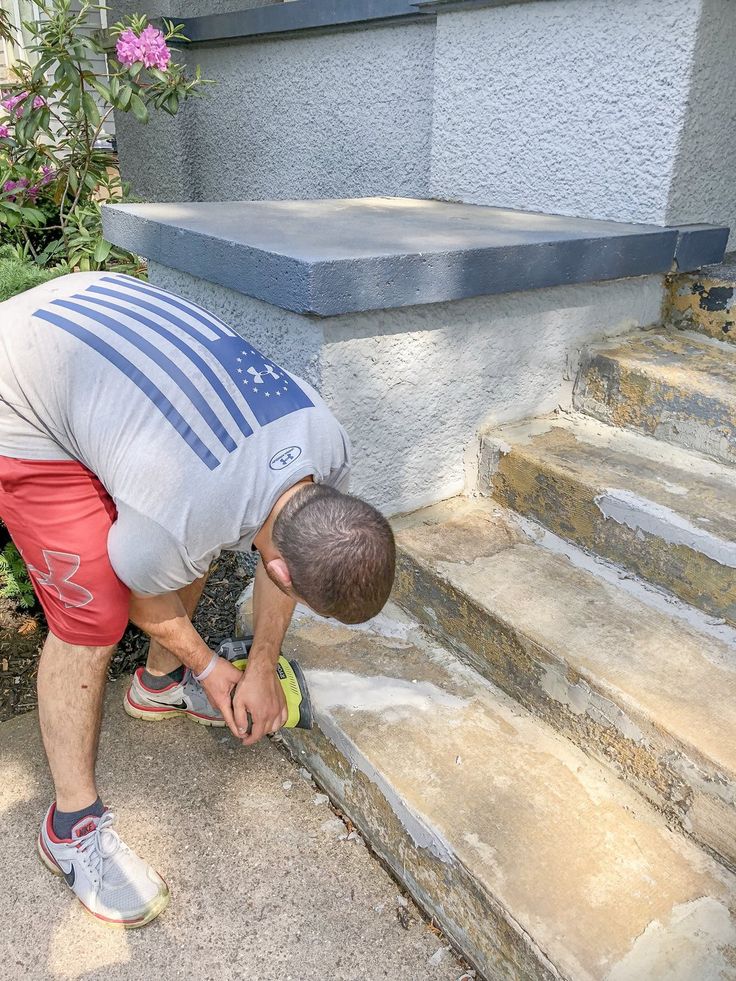 a man kneeling down to pick up something off the ground next to some steps and flowers