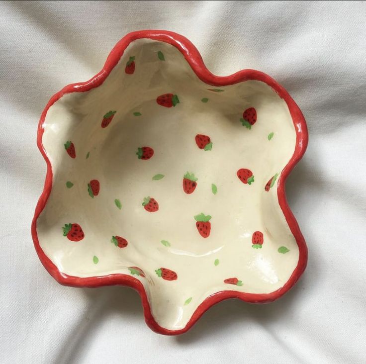 a red and white bowl with strawberries on it sitting on top of a bed