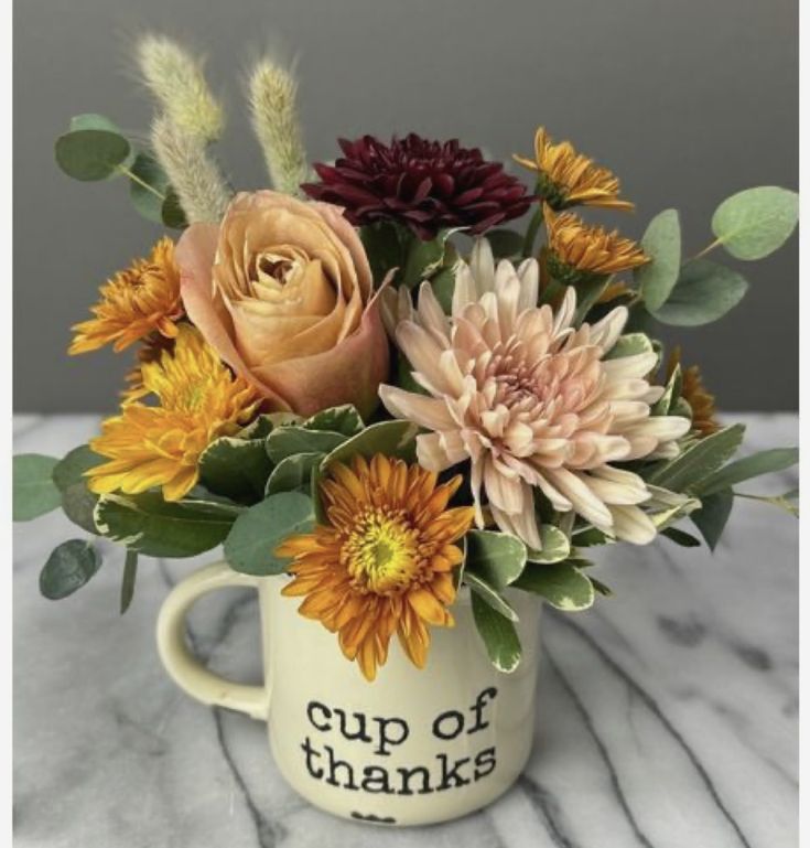 a coffee cup filled with flowers on top of a table