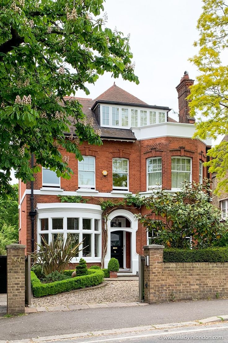 a large red brick house with white trim on the front and side windows, surrounded by greenery