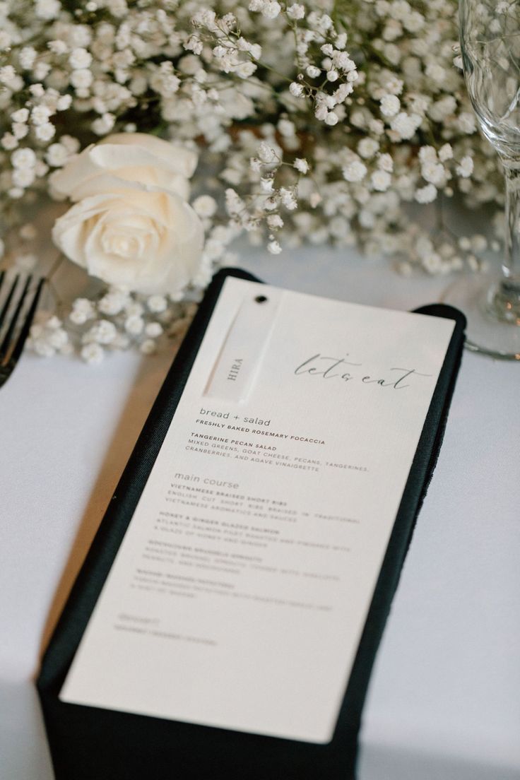 a menu sitting on top of a table next to a vase filled with white flowers