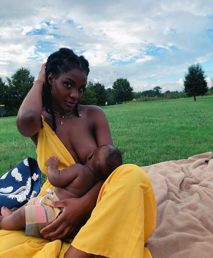 a woman holding a baby while sitting on top of a blanket