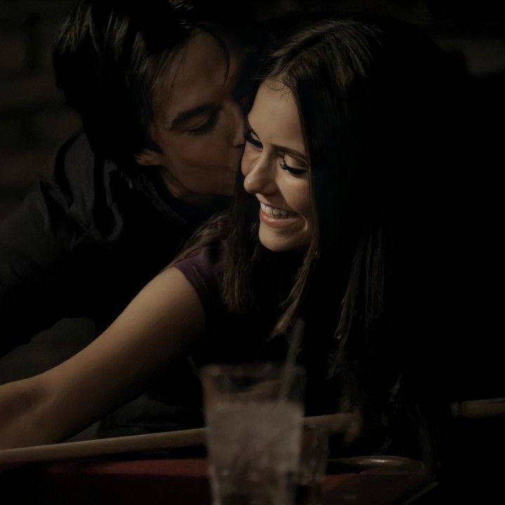 a young man and woman kissing in front of a table with a drink on it