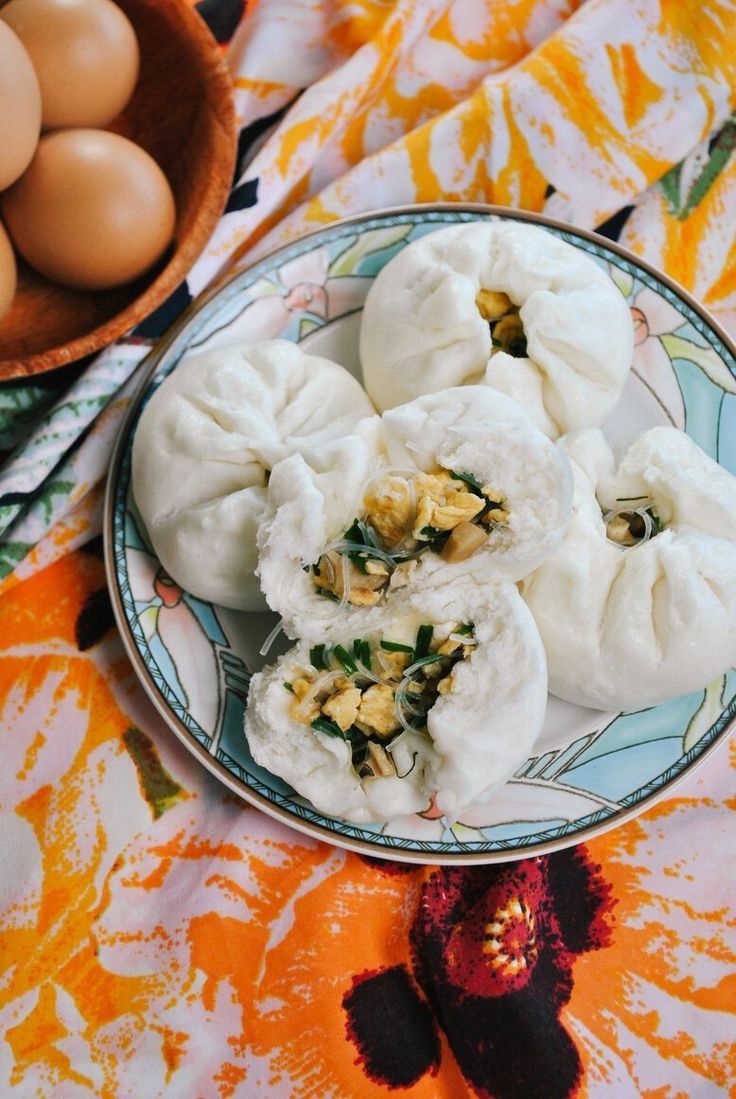 a plate with dumplings and eggs on a colorful table cloth next to a bowl