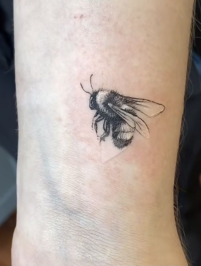 a small black and white bee tattoo on the ankle