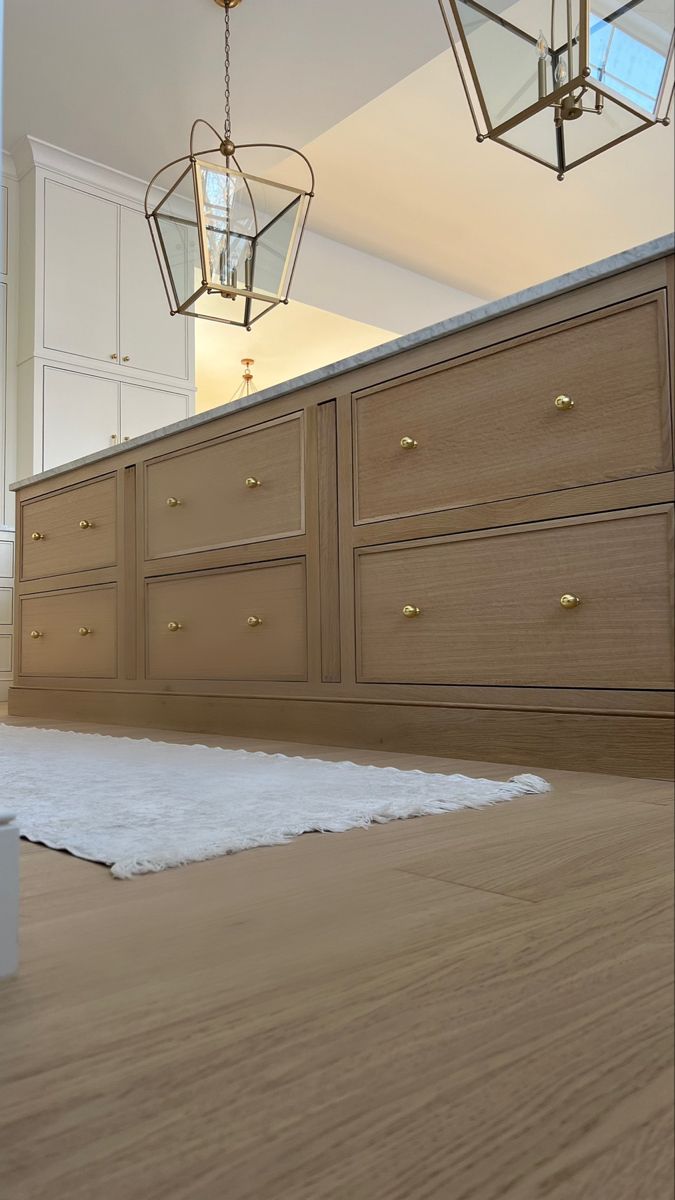 an empty kitchen with wooden floors and white cabinetry on the wall, chandeliers hanging from the ceiling