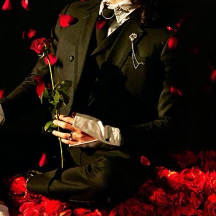 a man in a suit and tie holding a rose while sitting on a bed of roses